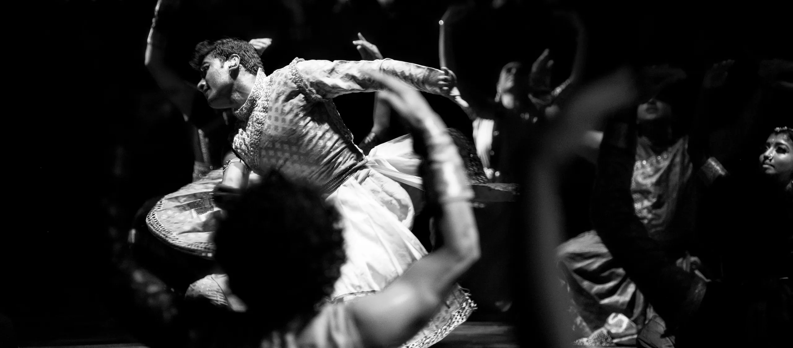 The same dancer leaning into a turn among the other dancers, with an arm blurred across the foreground