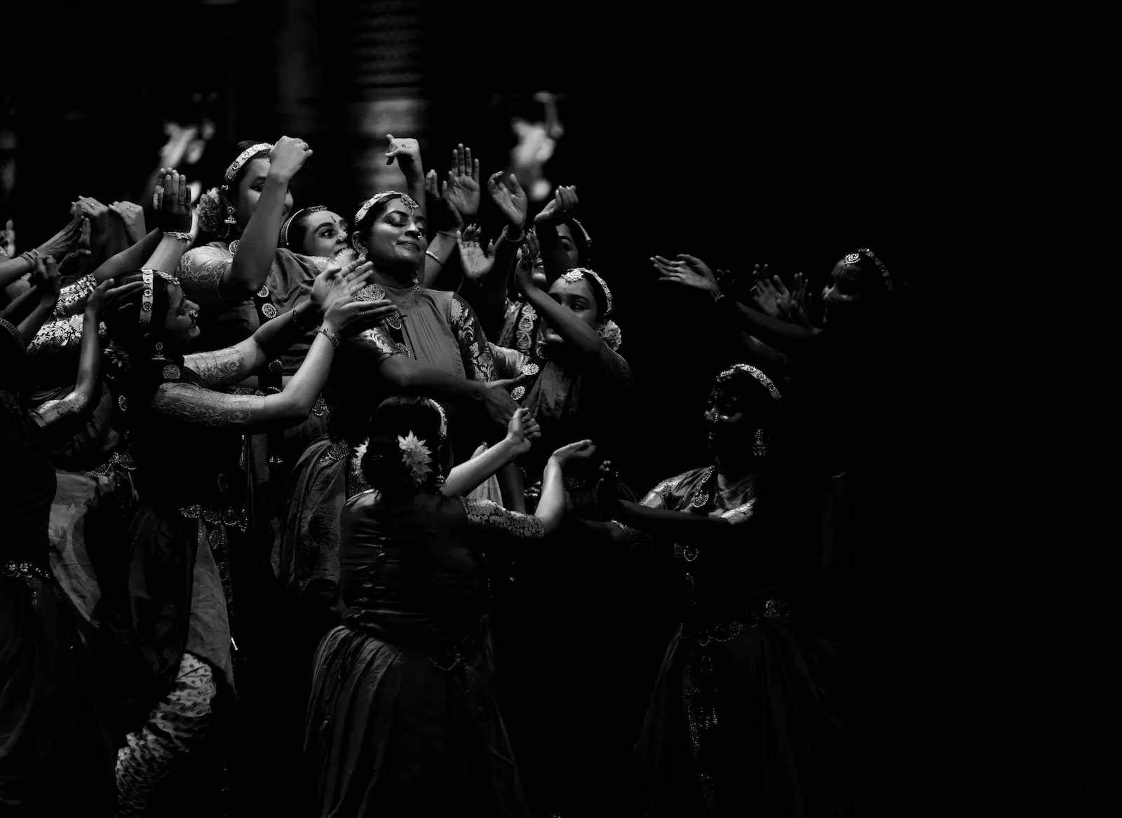 A group of dancers in costume reaching out towards one dancer in the middle, who has her eyes closed