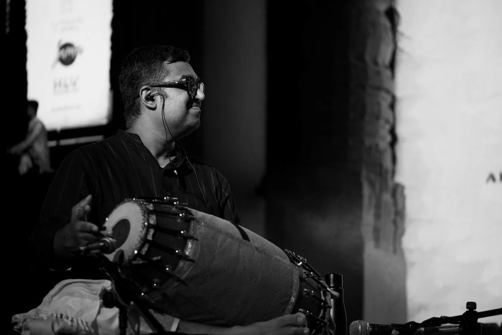A mridangam player in glasses, smiling as he plays