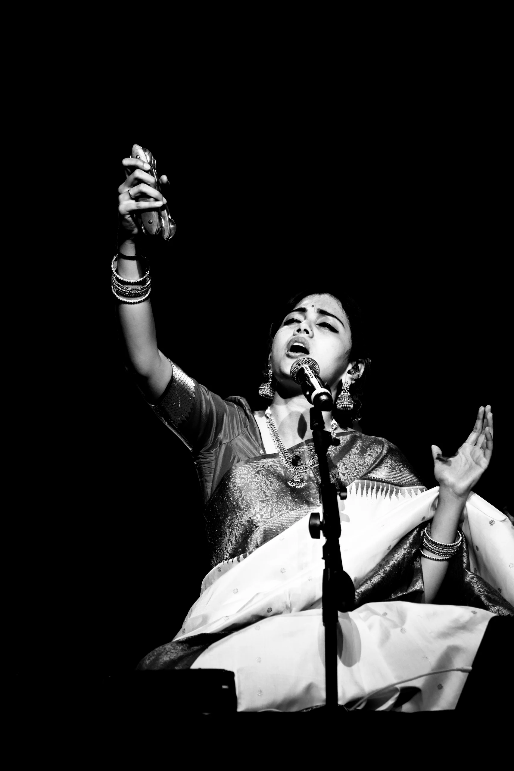 This is Sivasri Tejasvi Surya at the Bengaluru Ganesh Utsava, singing with her head tilted back, a pair of wooden clappers raised in one hand and the other hand open. It was the evening the entire crowd sang the bhajans along with her.