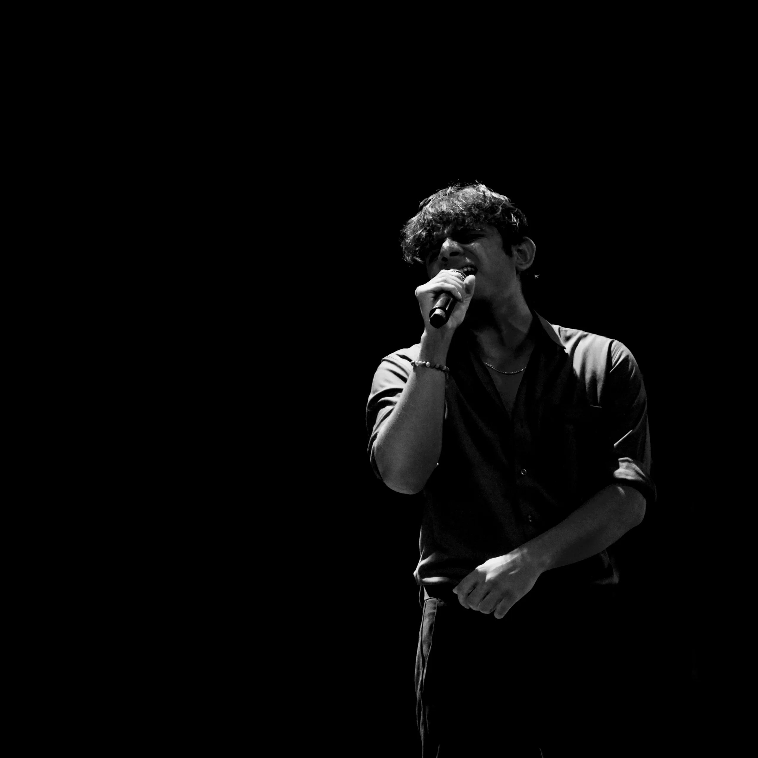 The singer is holding the note past the point where it would be comfortable to stop, with the microphone close enough to be part of the face, and everything outside the single spotlight is gone.