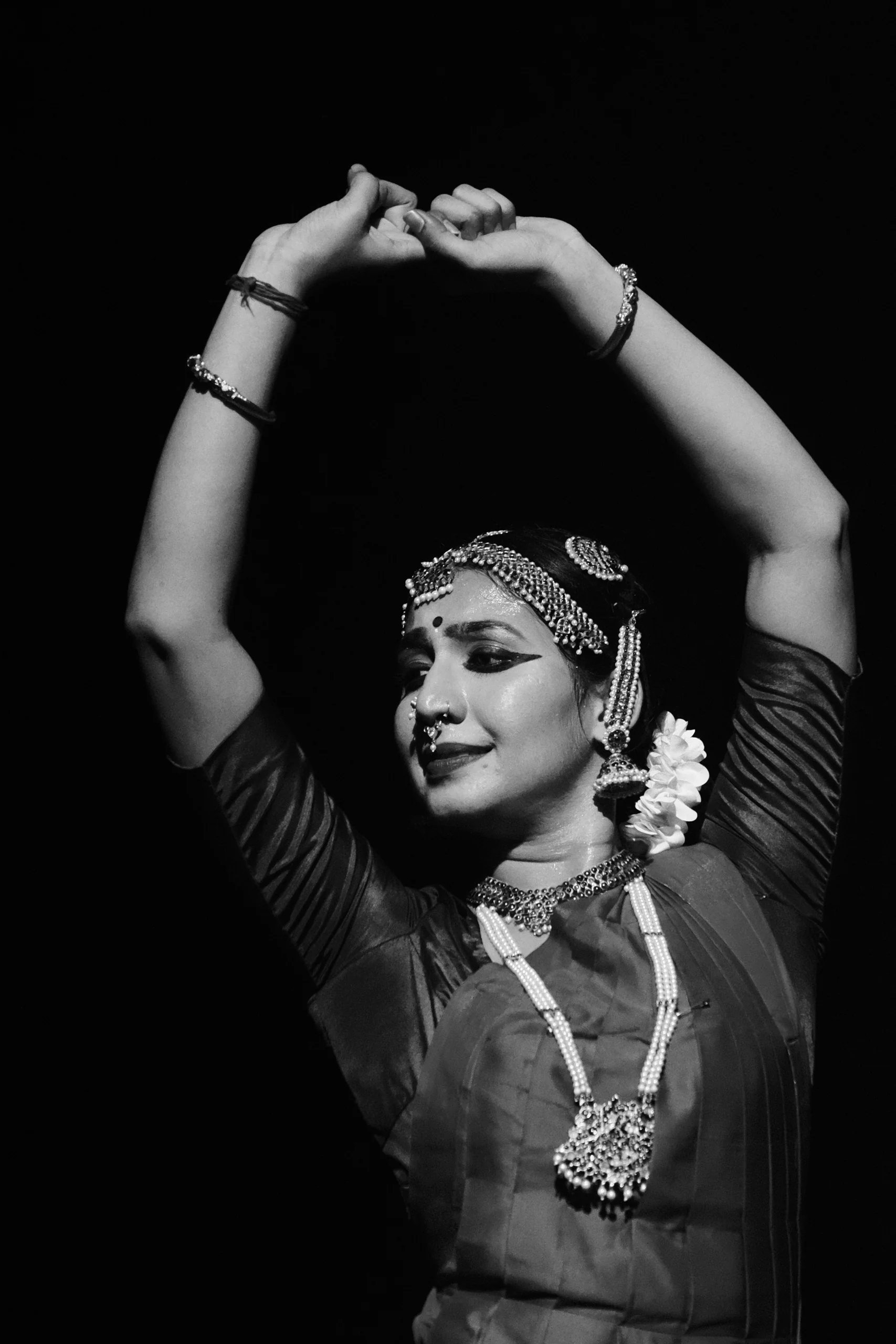 A dancer's hands are raised in a mudra that condenses years of practice into a gesture, with the face held in the half-second between effort and ease.