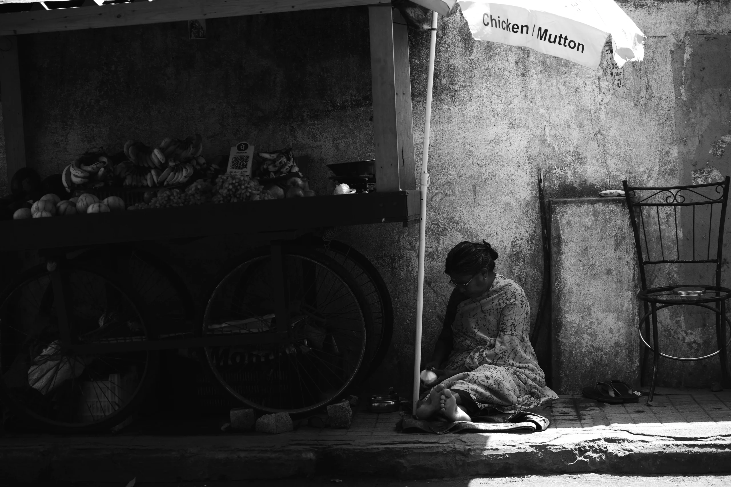 A vendor steals a quiet hour from the day's selling, pausing in the afternoon under a borrowed umbrella while the cart waits and the sun moves on.