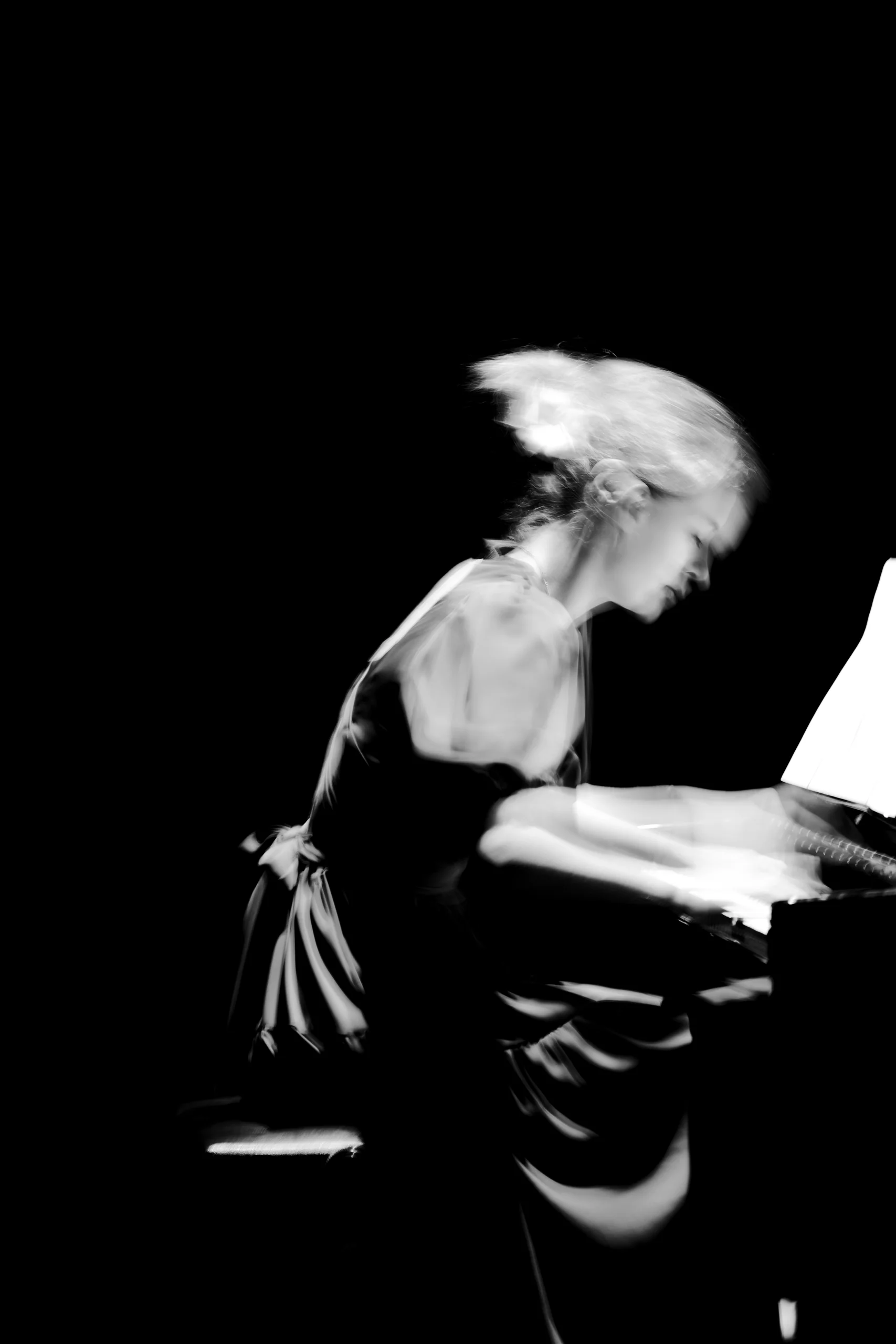 A long exposure of a piano recital, where the player blurs into the music itself while the score holds still on the stand.