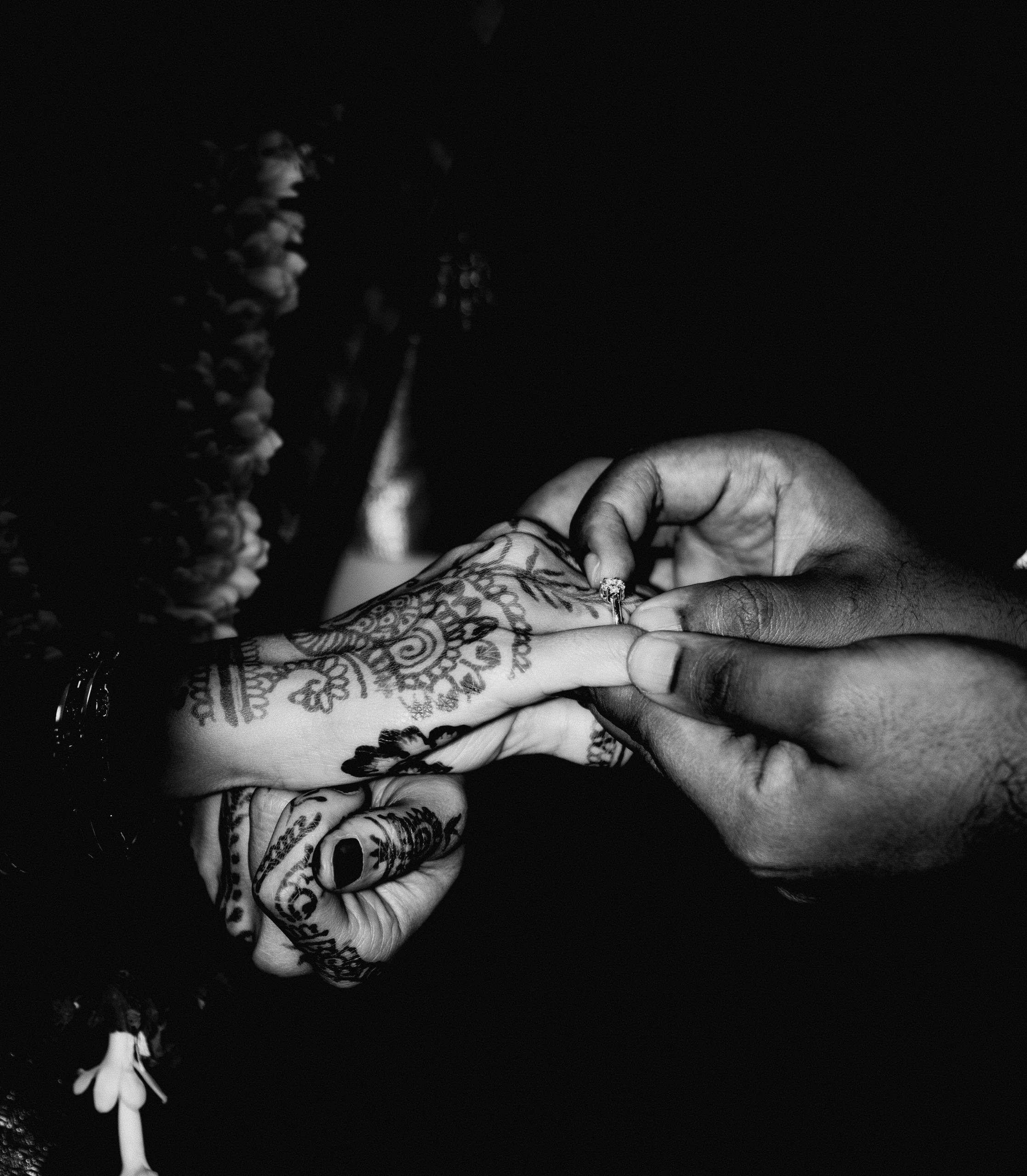 A ring slides onto a mehndi-covered hand, and all the ceremony around it falls into shadow, which leaves just the small, deliberate work of two pairs of hands and the promise passing between them.