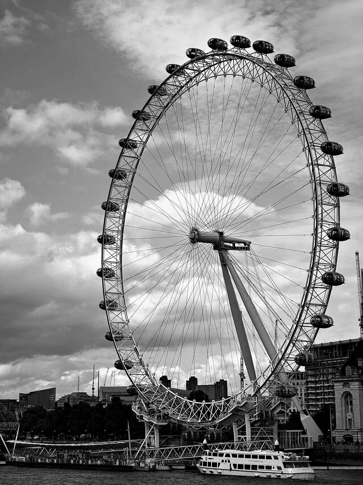 The London Eye against broken cloud, with a riverboat at the pier below