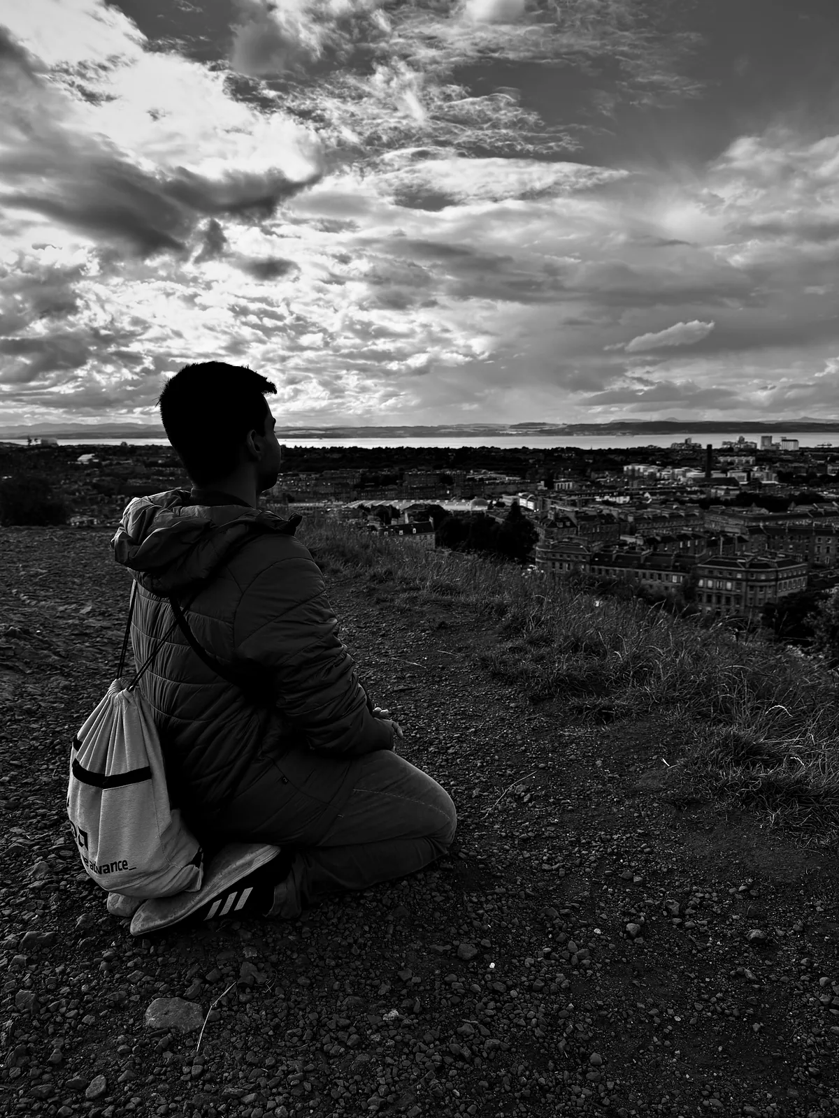 Me kneeling in vajrasana on the Calton Hill path, looking out over Edinburgh to the Firth of Forth