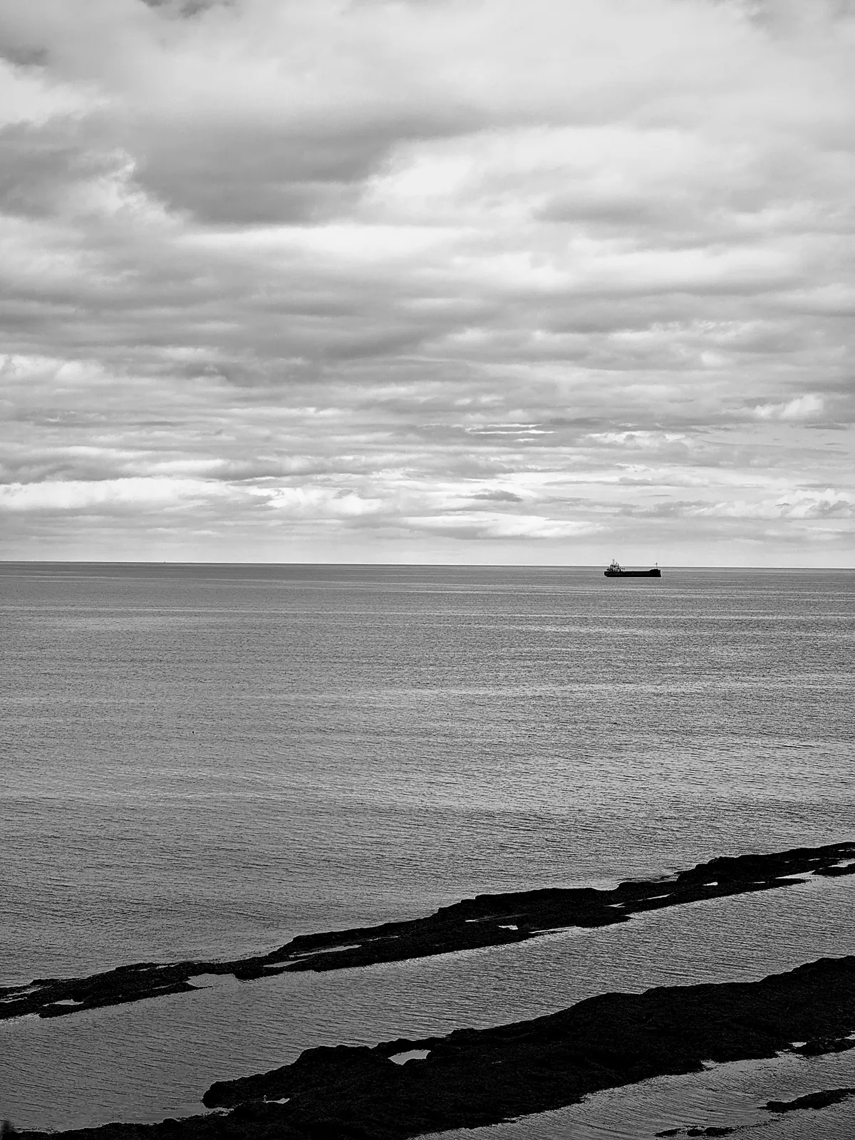 The North Sea off St Andrews with one ship on the horizon and dark rock ledges in front
