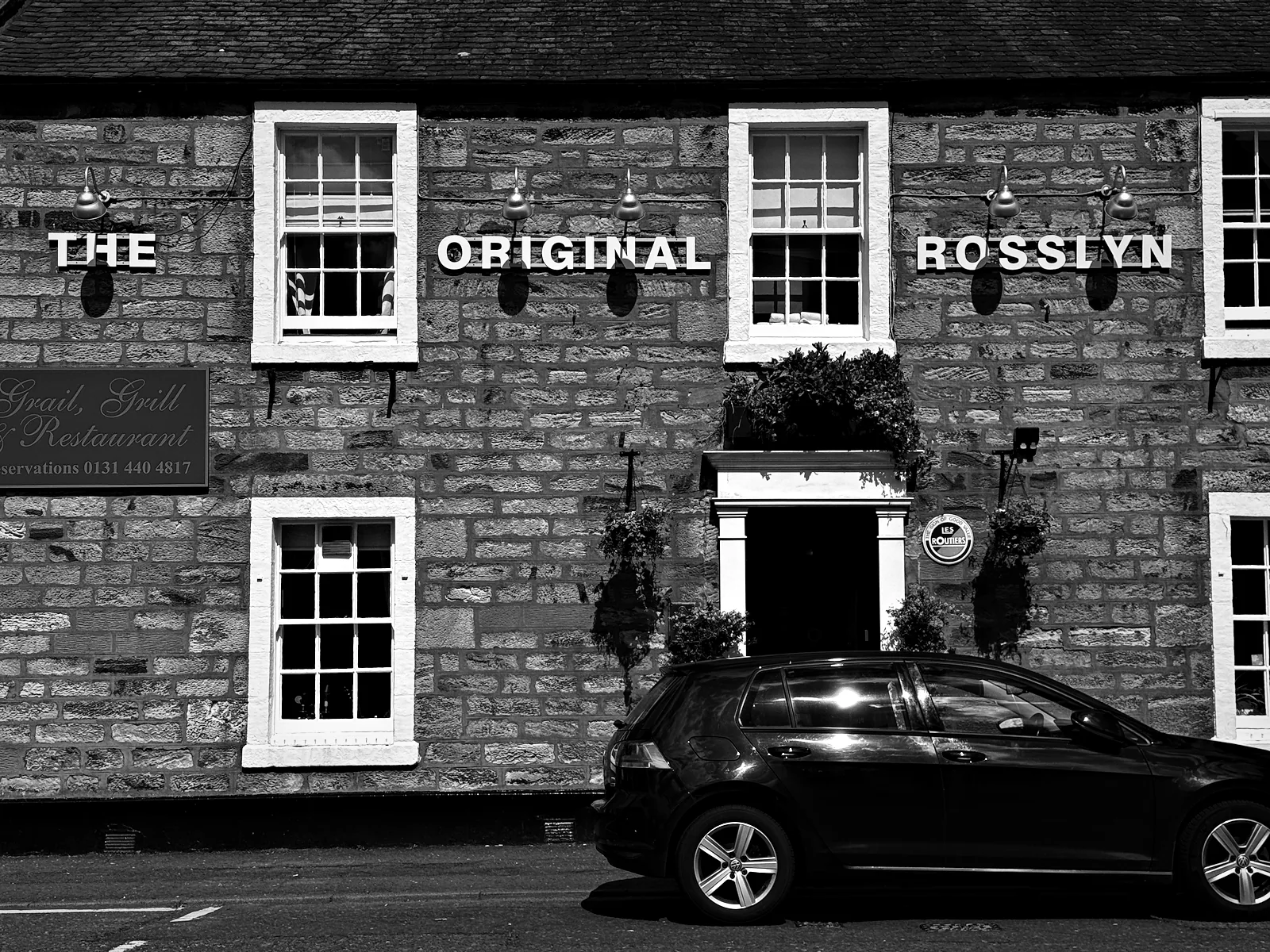 The stone front of The Original Rosslyn Inn in Roslin, its name in white letters between the windows, with a car parked outside