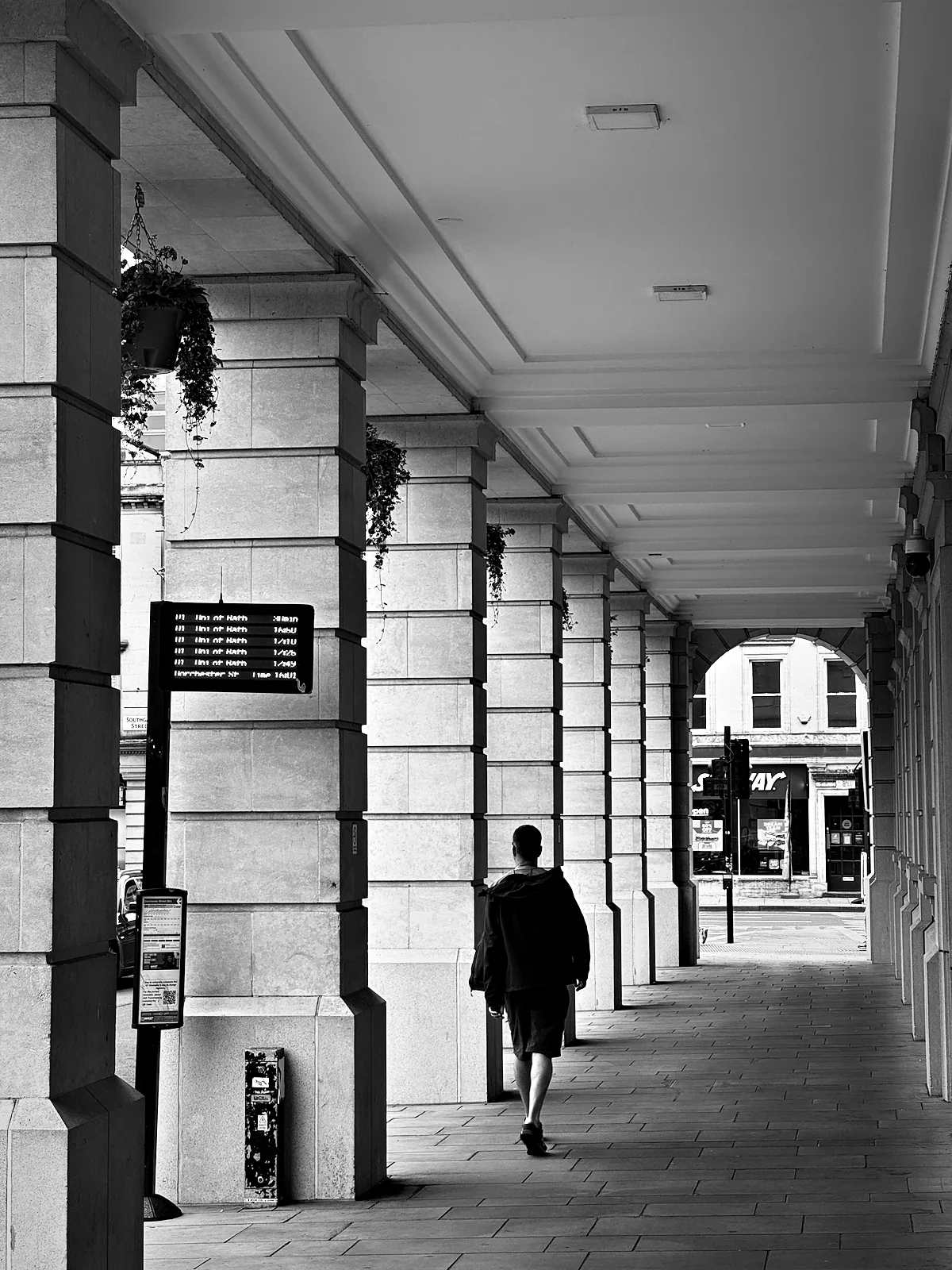 A man walking away down a stone colonnade in Bath