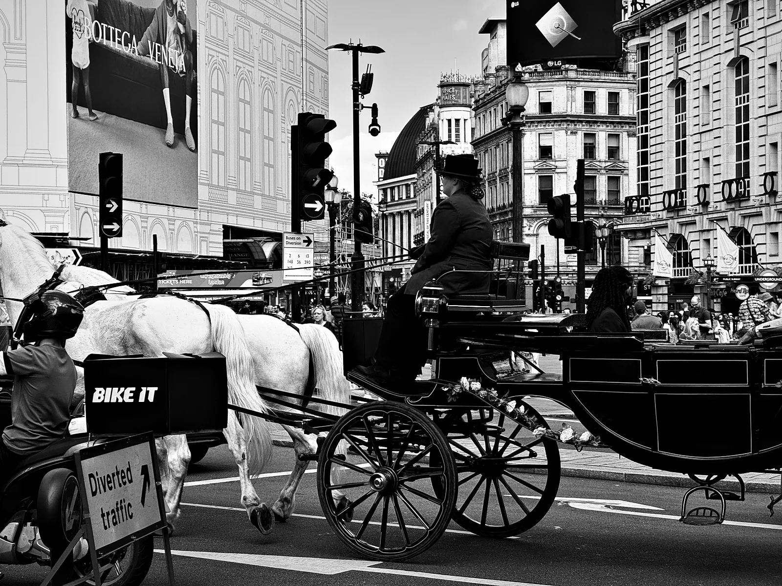 A horse-drawn carriage with a driver in a top hat passing through Piccadilly Circus